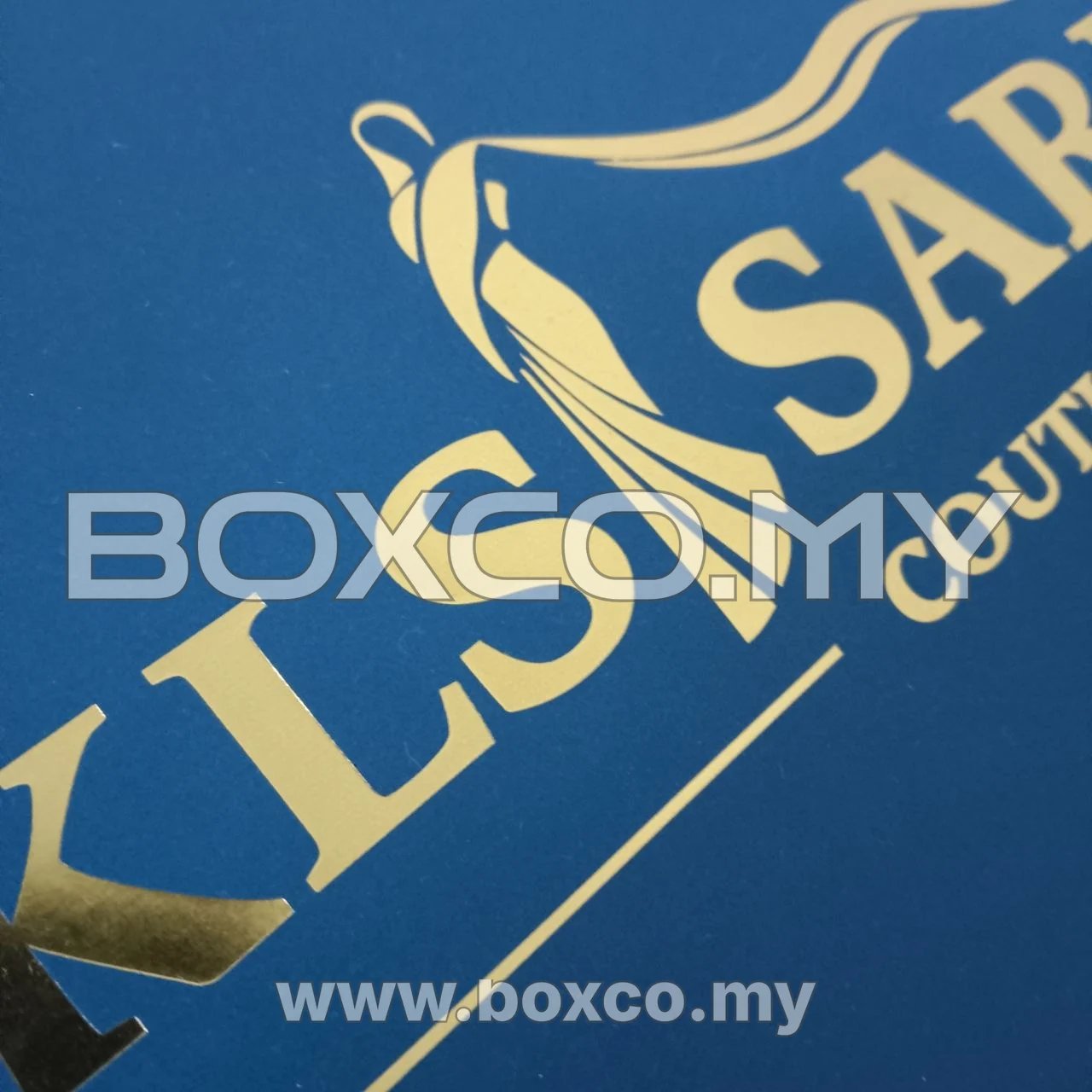 Close-up of gold lettering, linework and garment motif on dark green box lid
