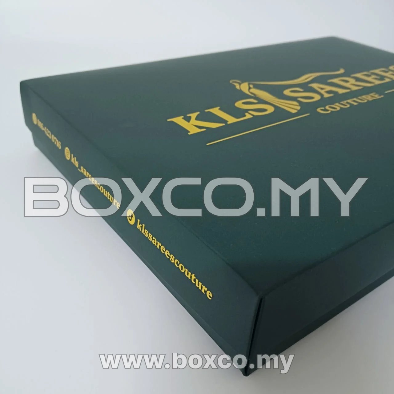 Closed dark green saree box with gold lid artwork and side-panel details