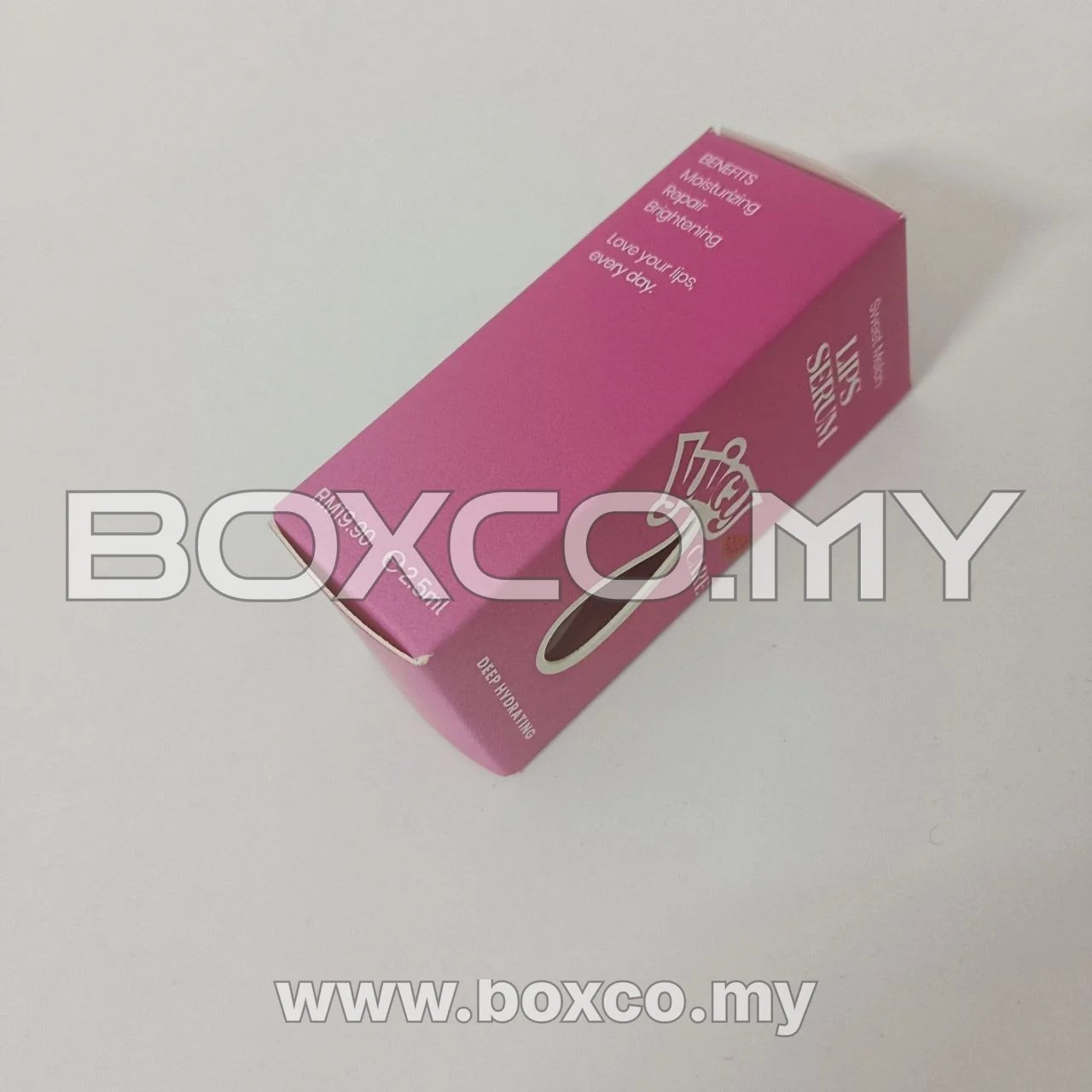 Angled side view of a pink lip serum carton showing its printed benefits panel